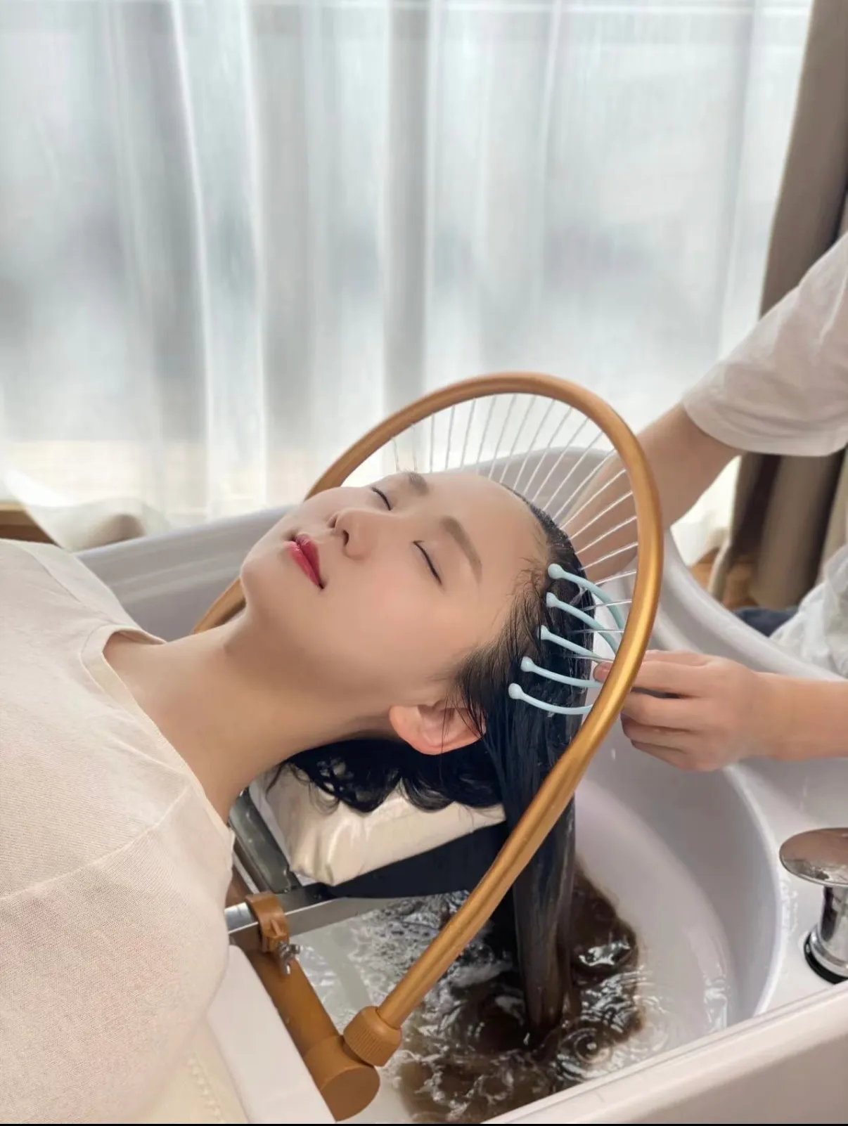 A guest reclined in the head spa basin at Aura in Issaquah, hair fanned out beneath the gold ring above the basin while warm water runs through it