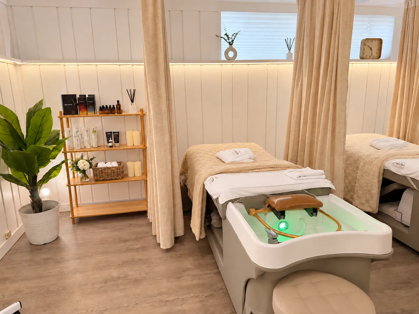 The treatment room at Aura in Issaquah: cream panelling, a warm light ledge, a shelf of products and candles, and a basin lit at the foot of the bed